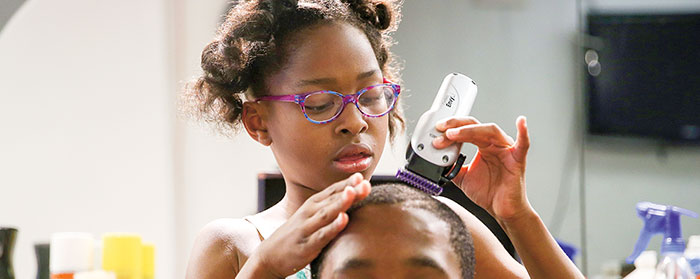 a young girl using clippers to a give a boy a haircut