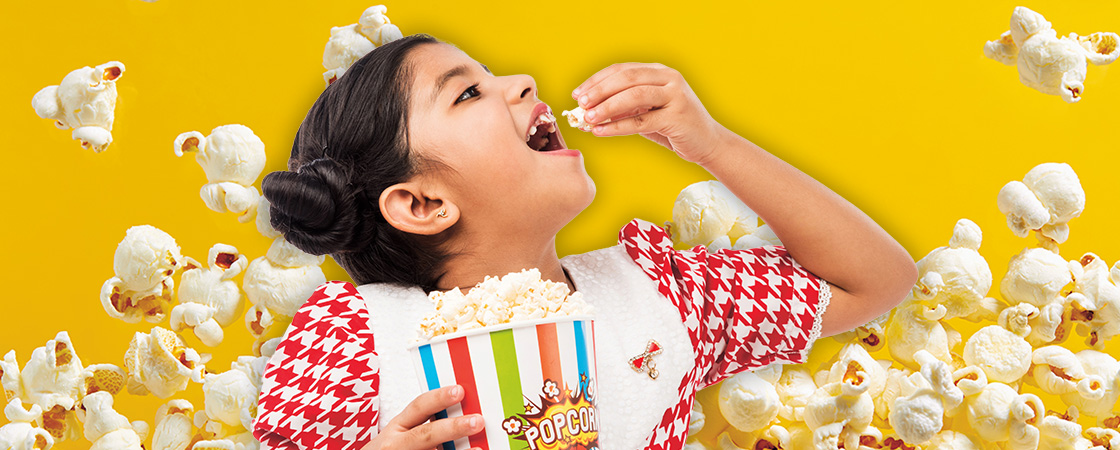 Child eating popcorn in front of a yellow popcorn background